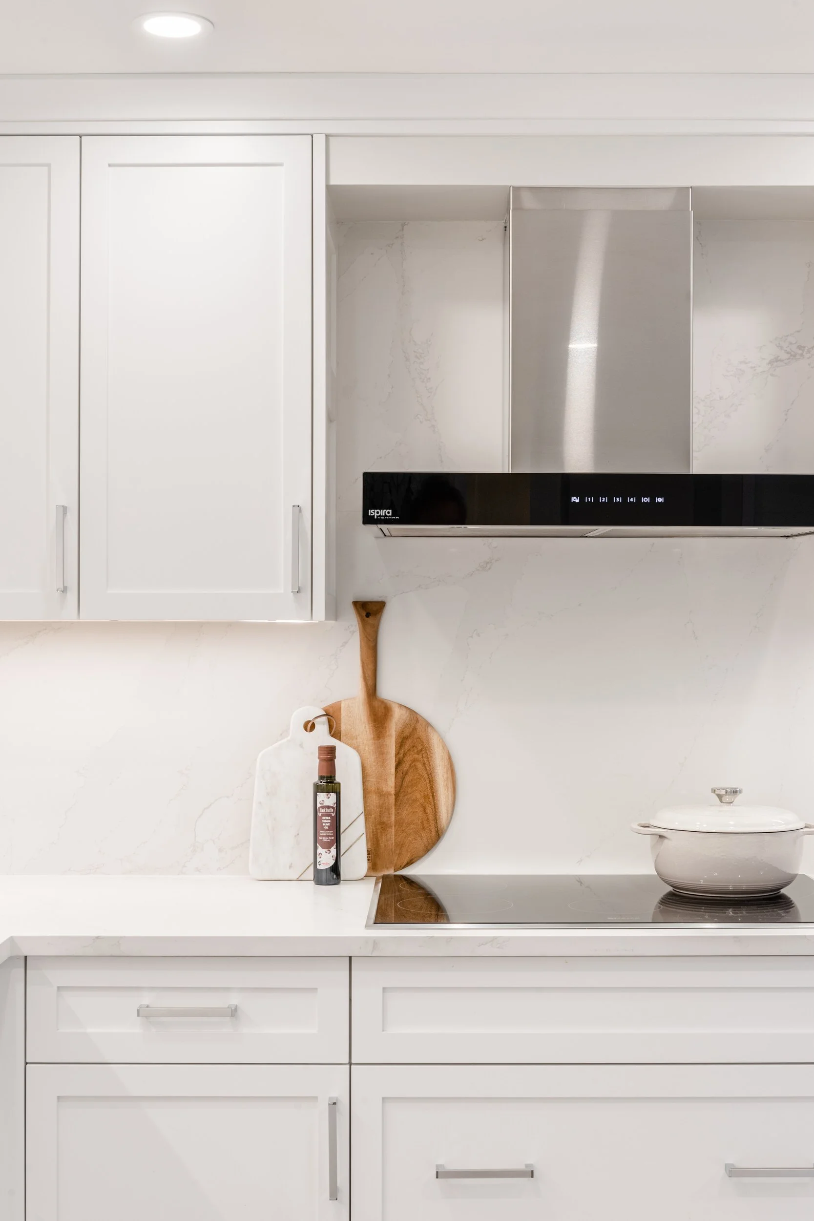 White kitchen with cabinetry, marble backsplash, wooden and marble cutting boards, and a white pot on the stove.
