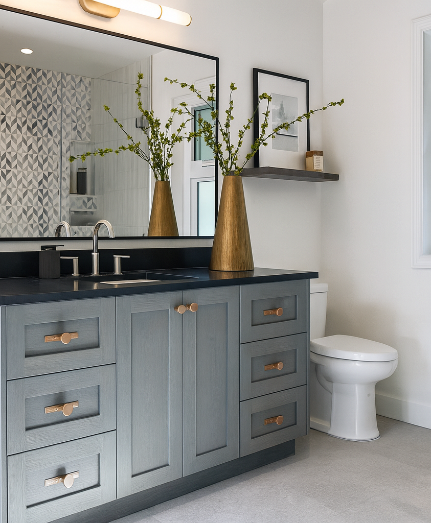 Modern bathroom vanity with black countertop, wooden drawers, a large mirror, decorative black vase with dried branches, and toiletries, against white walls with hanging gray towels.