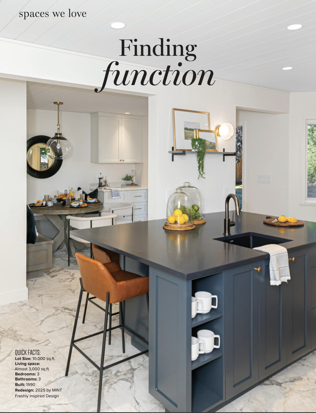Interior view of a modern kitchen with a navy blue island, black countertop, and white cabinetry in the background. Decor includes lemon and lime displays under glass cloches, hanging pendant light, wall art, and open shelving with white mugs. Quick facts about the house are listed in the lower left corner.