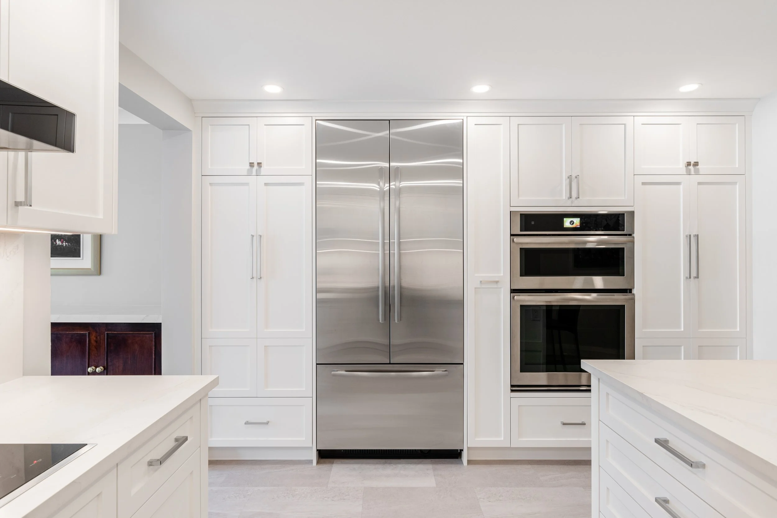 Modern white kitchen with stainless steel refrigerator and double wall ovens.