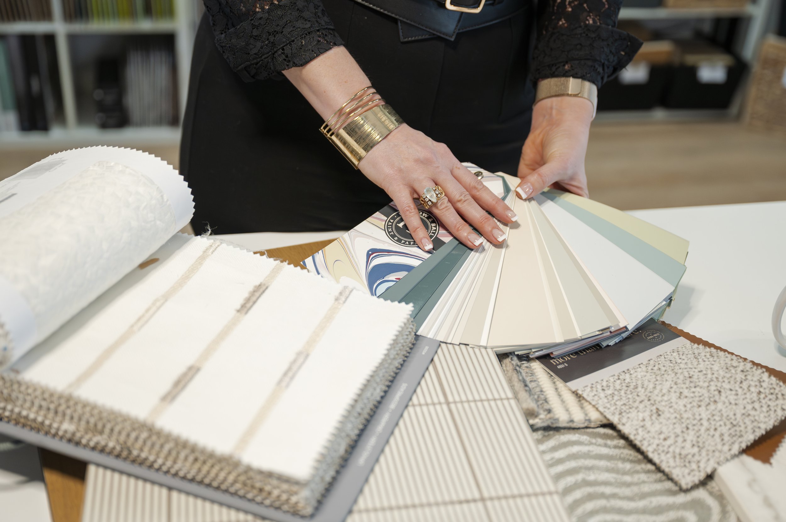 Victoria interior designer flipping through colour and fabric sample books with design materials spread across a table.