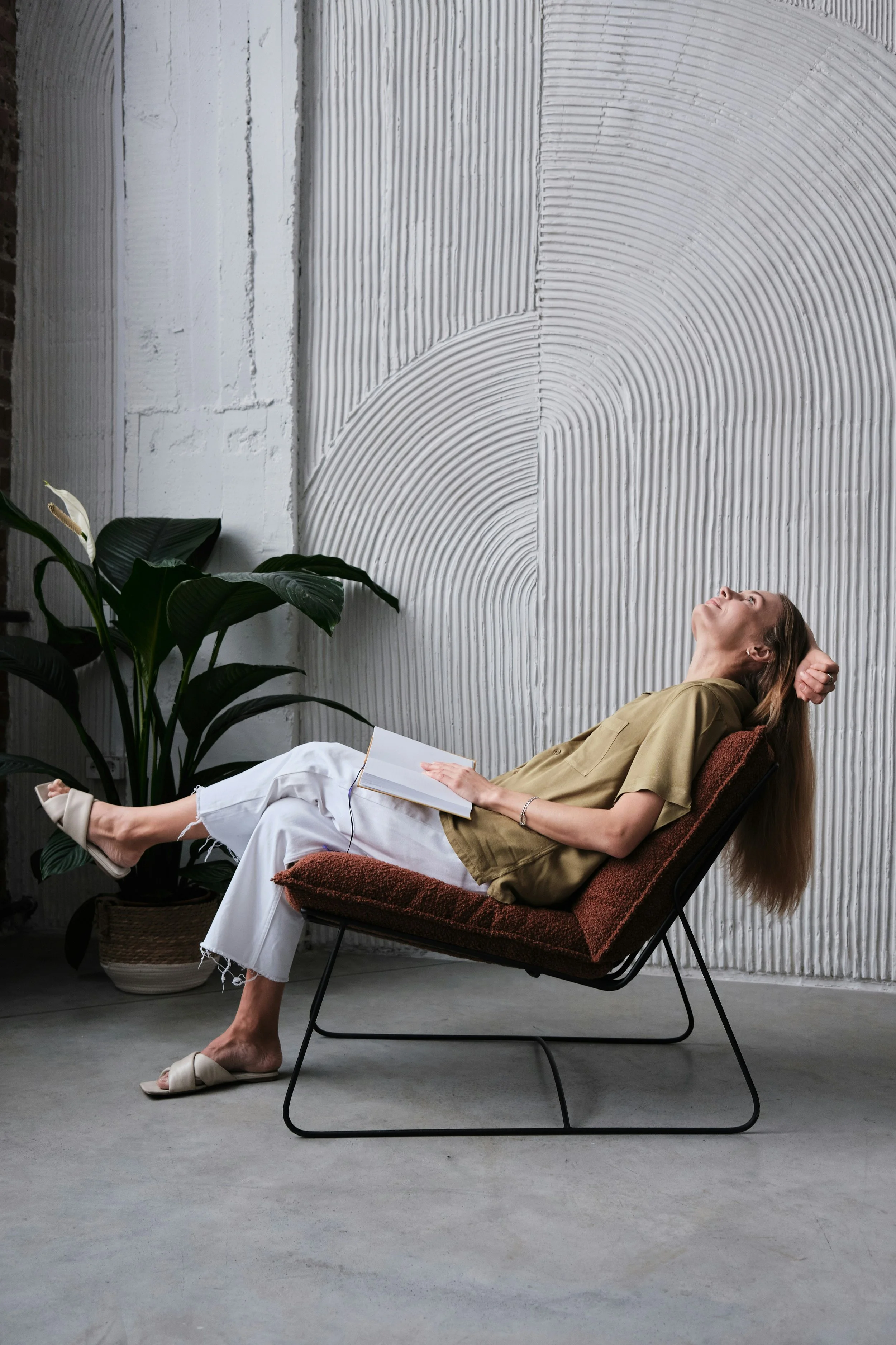 Women sitting in a modern chair, holding an open book, looking up | Progesterone affects everything
