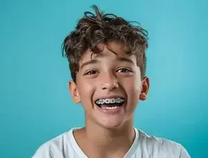 Close-up of a boy with curly hair smiling and showing braces on his teeth, against a blue background.