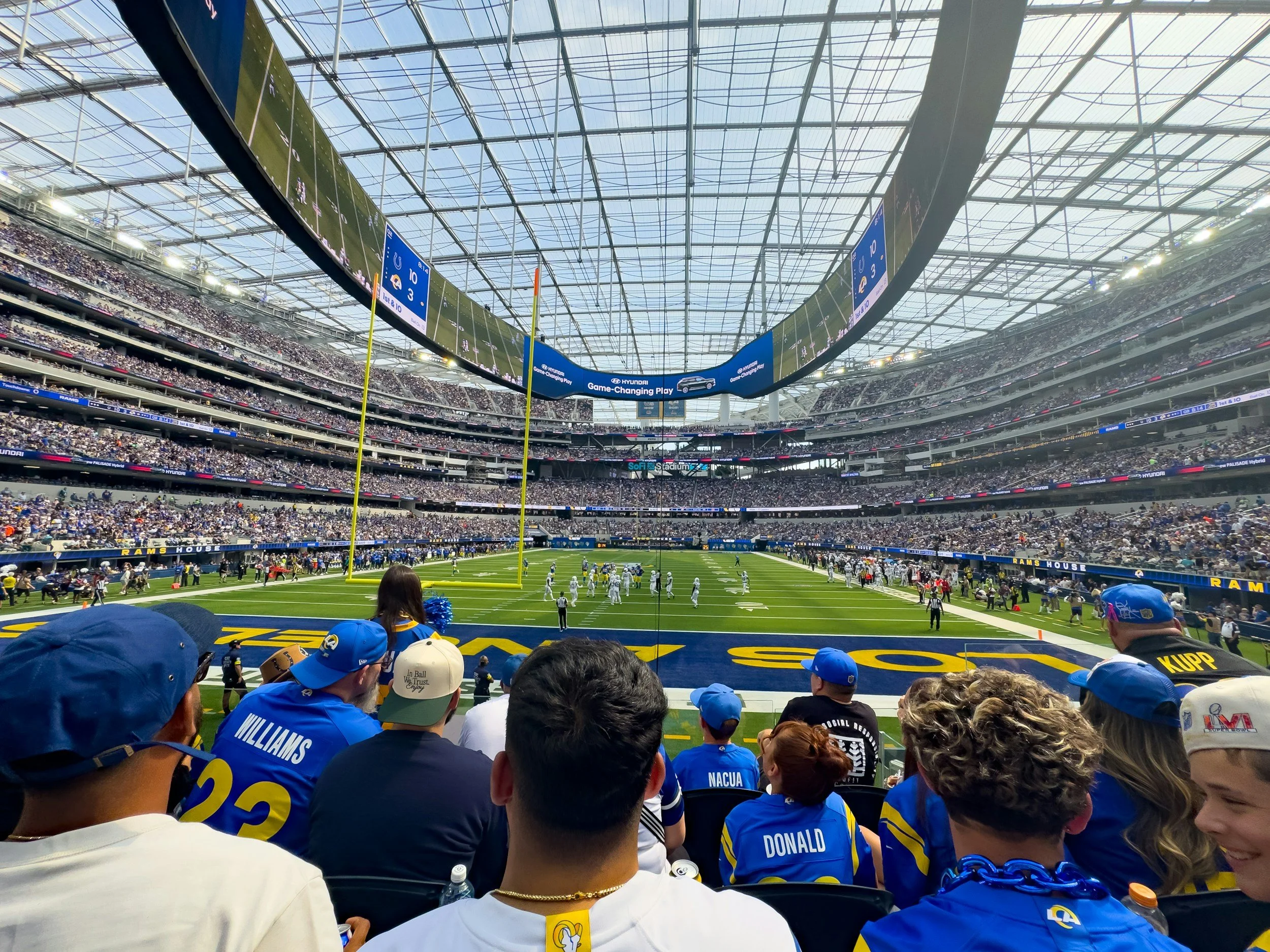 View of an indoor football stadium with players on the field, spectators in the stands, and a large scoreboard overhead, during a game.