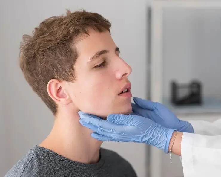 Young male patient getting throat examined by healthcare professional wearing gloves.