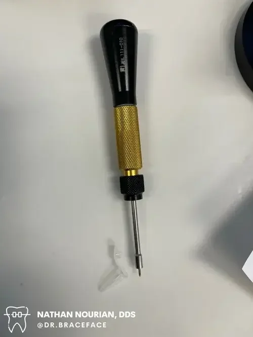 A precision screwdrivers with a black handle, gold knurled grip, and a metal shaft placed on a white surface.