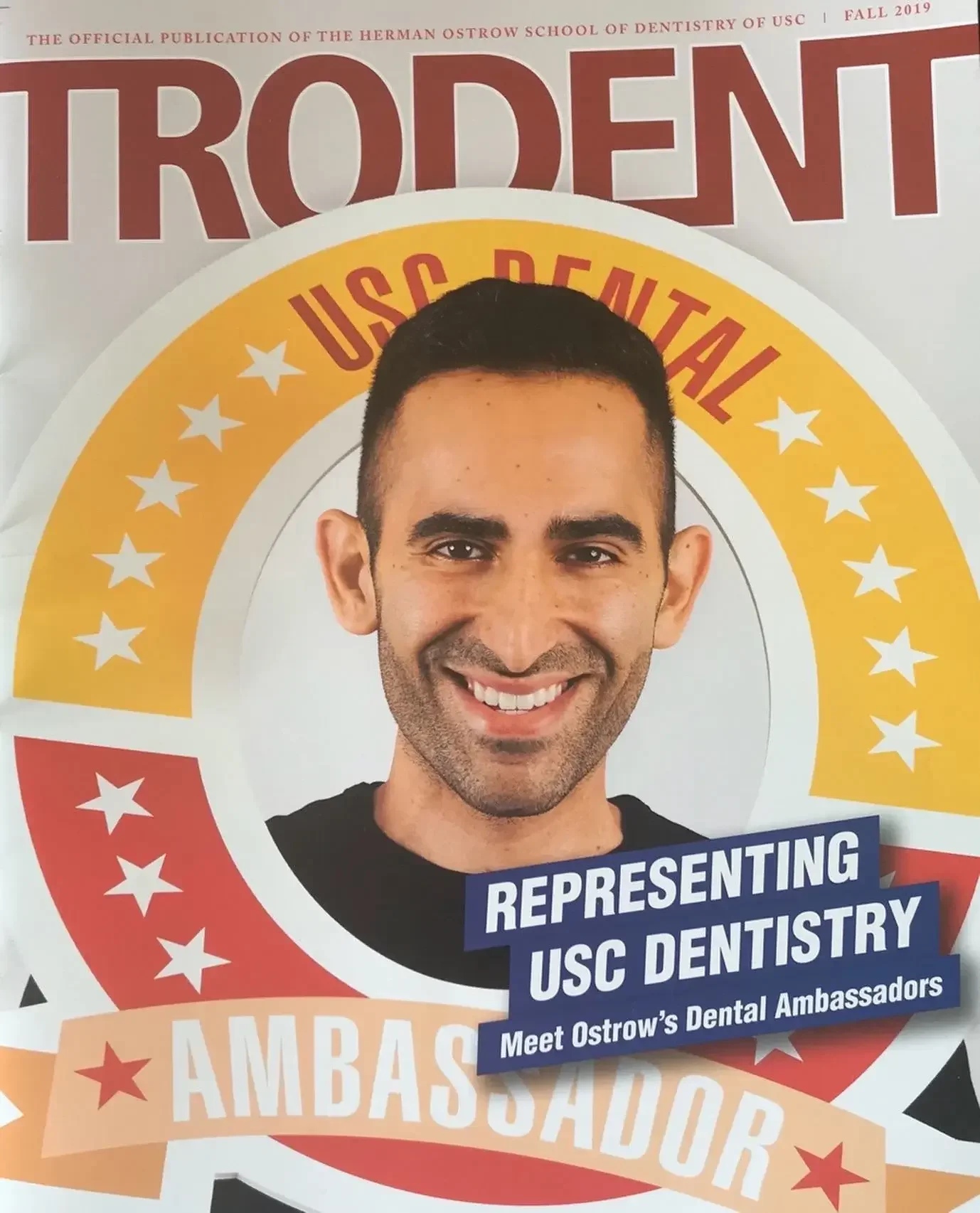 A poster featuring a smiling man with dark hair, promoting the USC Dental Ambassadors program. The poster has a circular design with red, yellow, and white colors and text that says 'Representing USC Dentistry' and 'Meet Ostrow's Dental Ambassadors'.