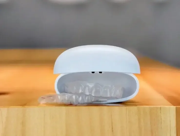 White oval-shaped case with transparent plastic dental retainers inside, placed on a wooden surface.