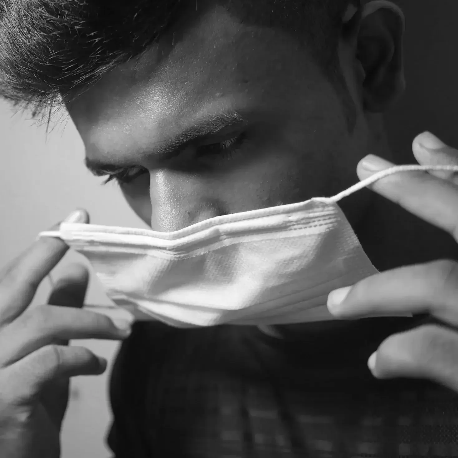 A young man is putting on a face mask, holding it with both hands, with a pressurized, serious expression.