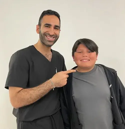 A man in scrubs smiling and pointing at a young boy smiling and wearing a jacket.