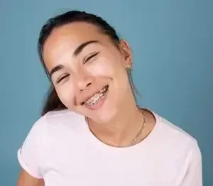 Smiling young girl with braces and long dark hair against a blue background.