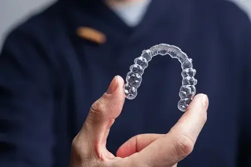 Person holding a clear dental aligner or retainer.