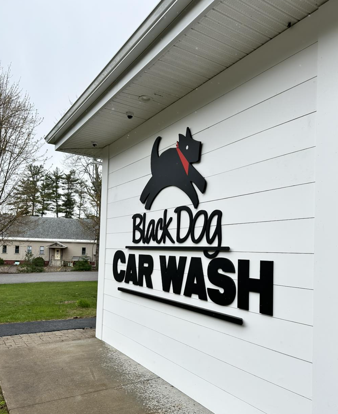 A sign for Black Dog Car Wash featuring a black dog illustration with a red collar on a white building exterior.