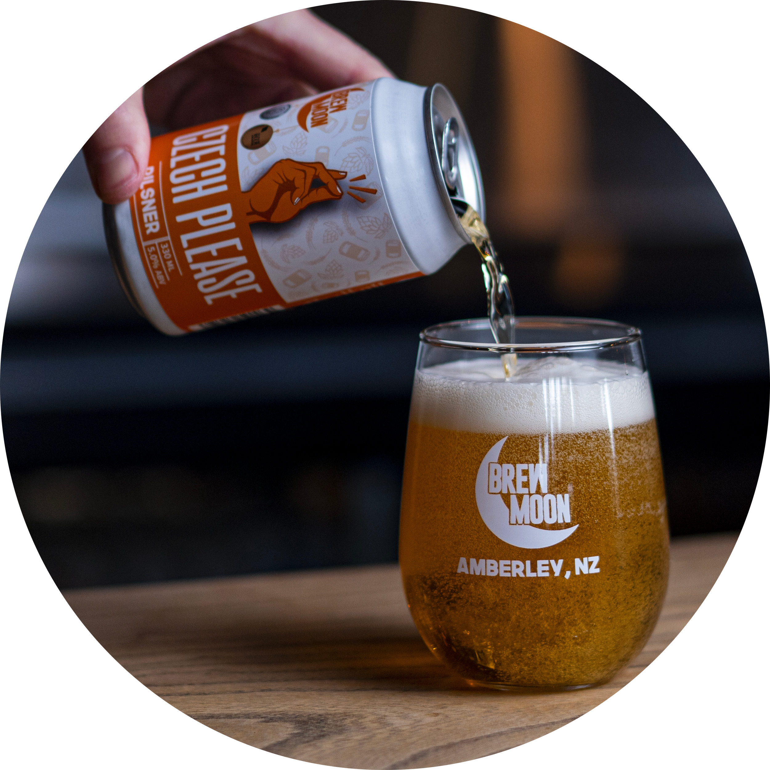 Hand pouring Brew Moon Czech Pilsner from a can into a Brew Moon branded glass on a wooden bar in Amberley, New Zealand