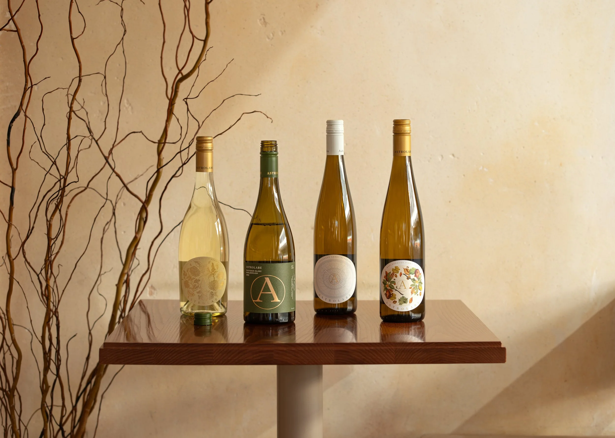 Astrolabe Wines range displayed on a wooden table with four Marlborough white wine bottles against a neutral styled backdrop