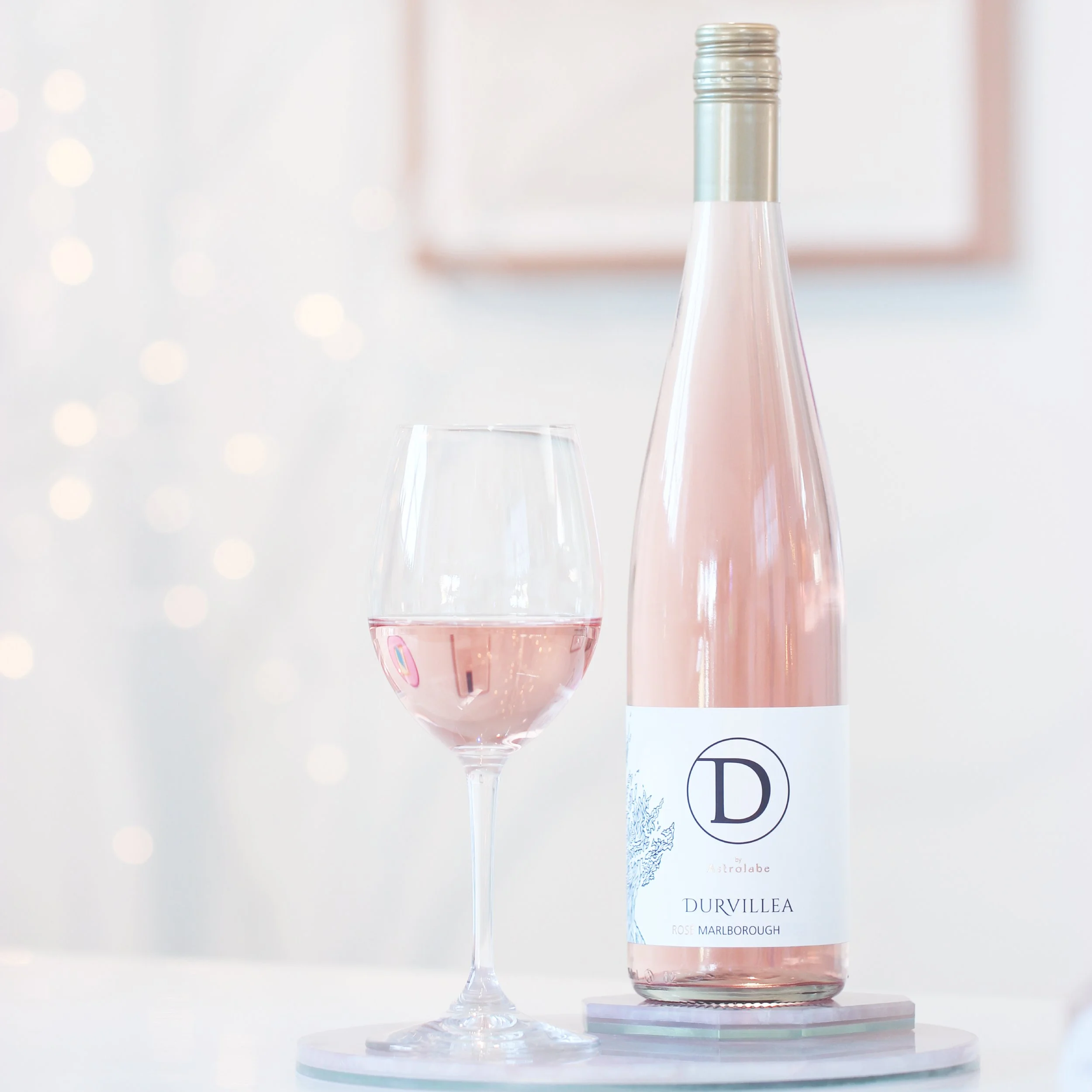 Durvillea Rosé bottle and glass of pale pink wine on a light, minimalist background with soft bokeh lights.