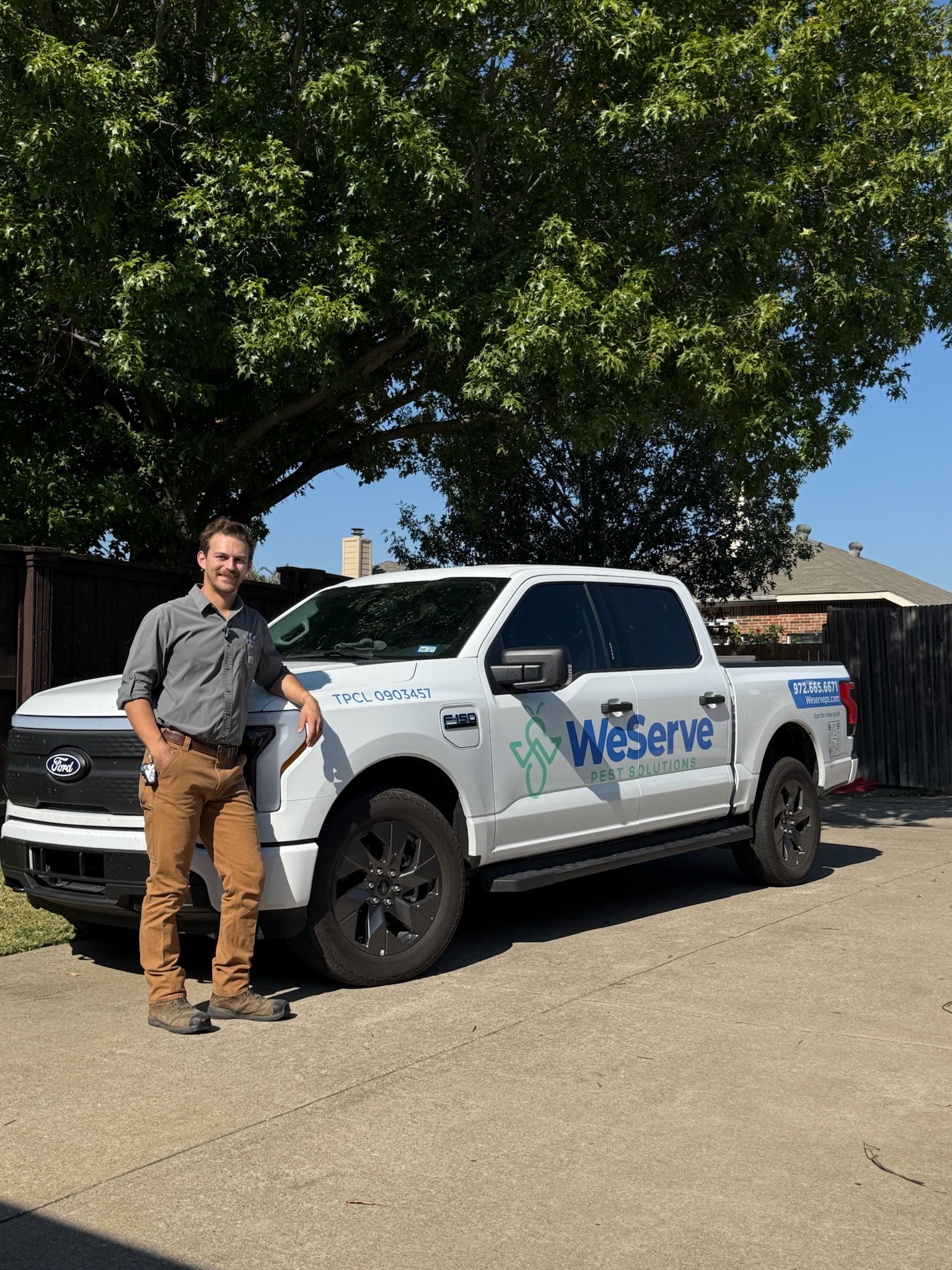 A man standing next to a white Ford F-150 pickup truck with 'WeServe Pest Solutions' logo on the side, parked on a driveway with a large tree in the background.