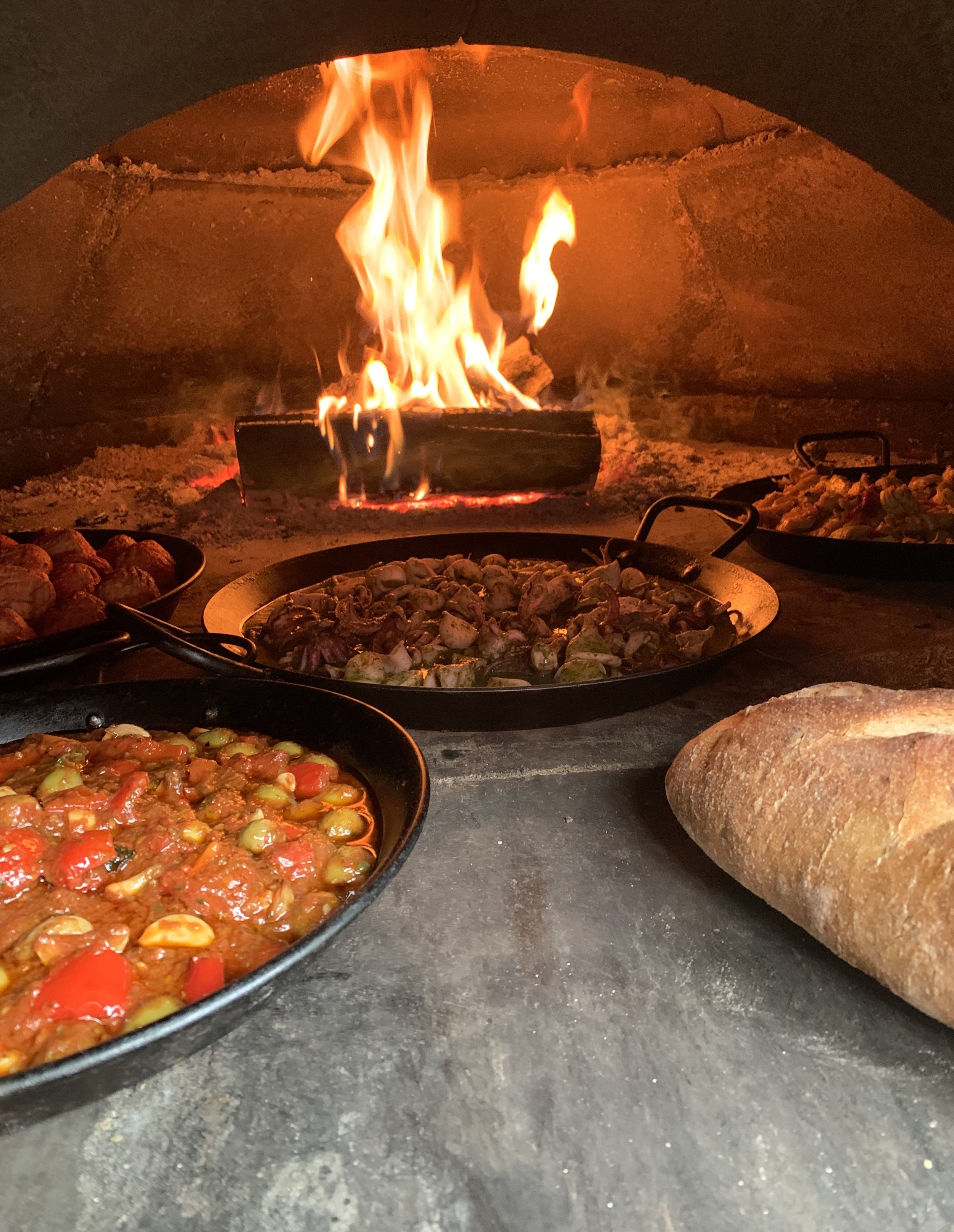 Various pans of food cooking in a pizza oven