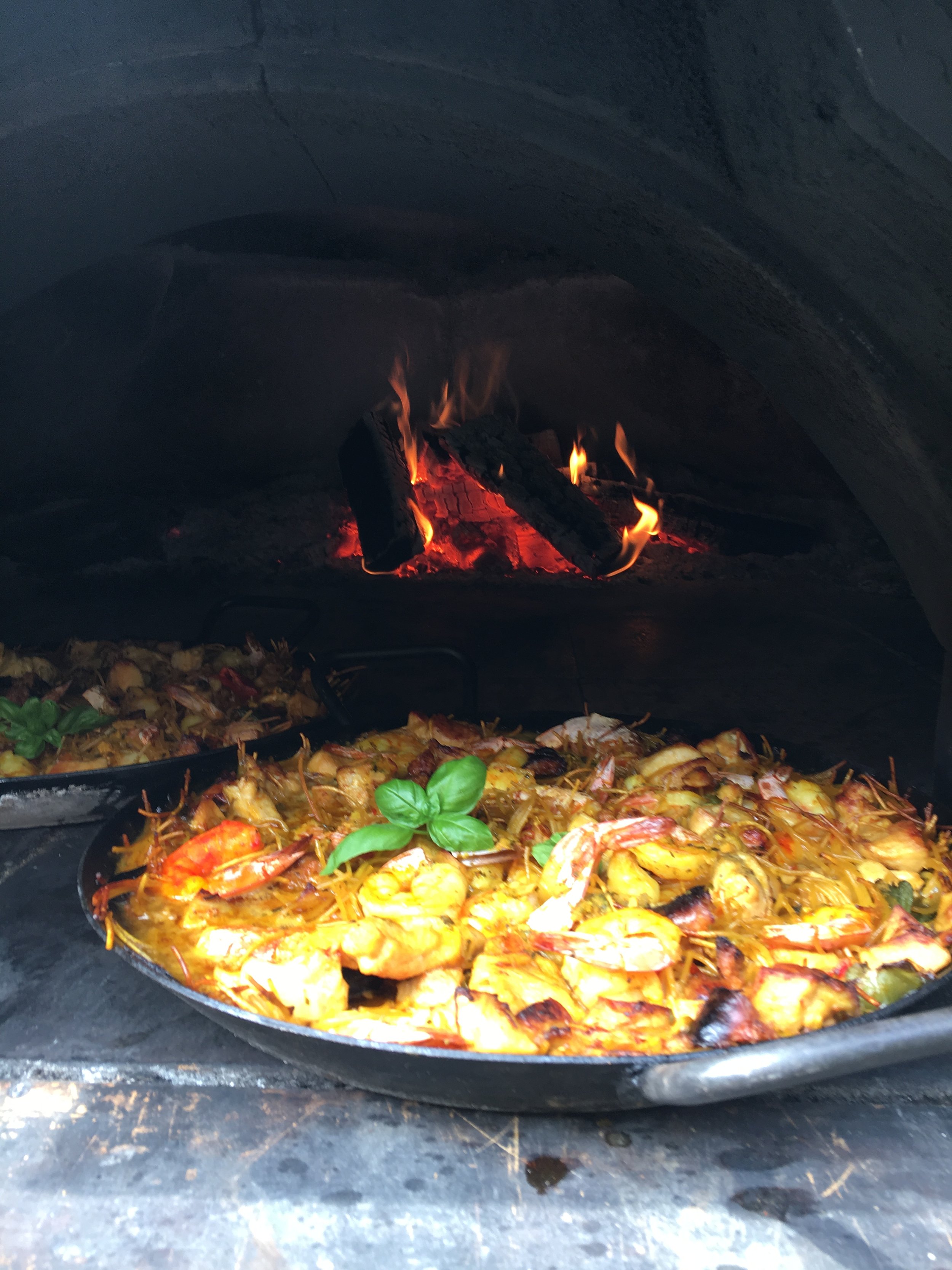More various pans of food being cooked in a pizza oven