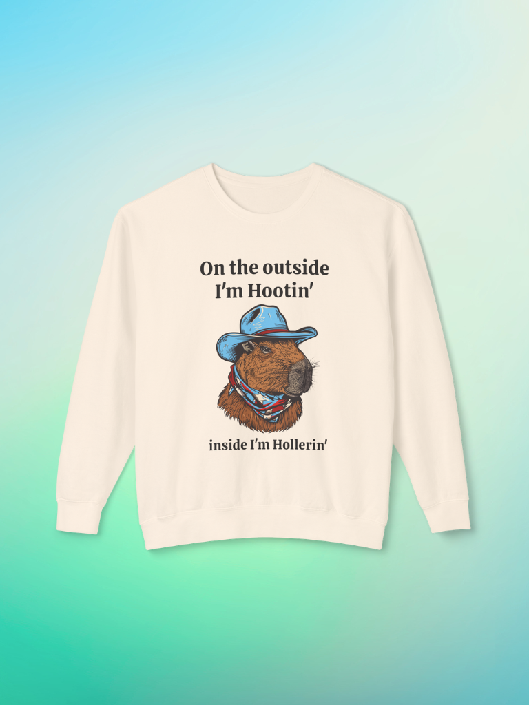 Ivory crewneck sweatshirt featuring a colorful illustration of a capybara wearing a blue cowboy hat and bandana, with text that reads ‘On the outside I’m Hootin’, inside I’m Hollerin’.’