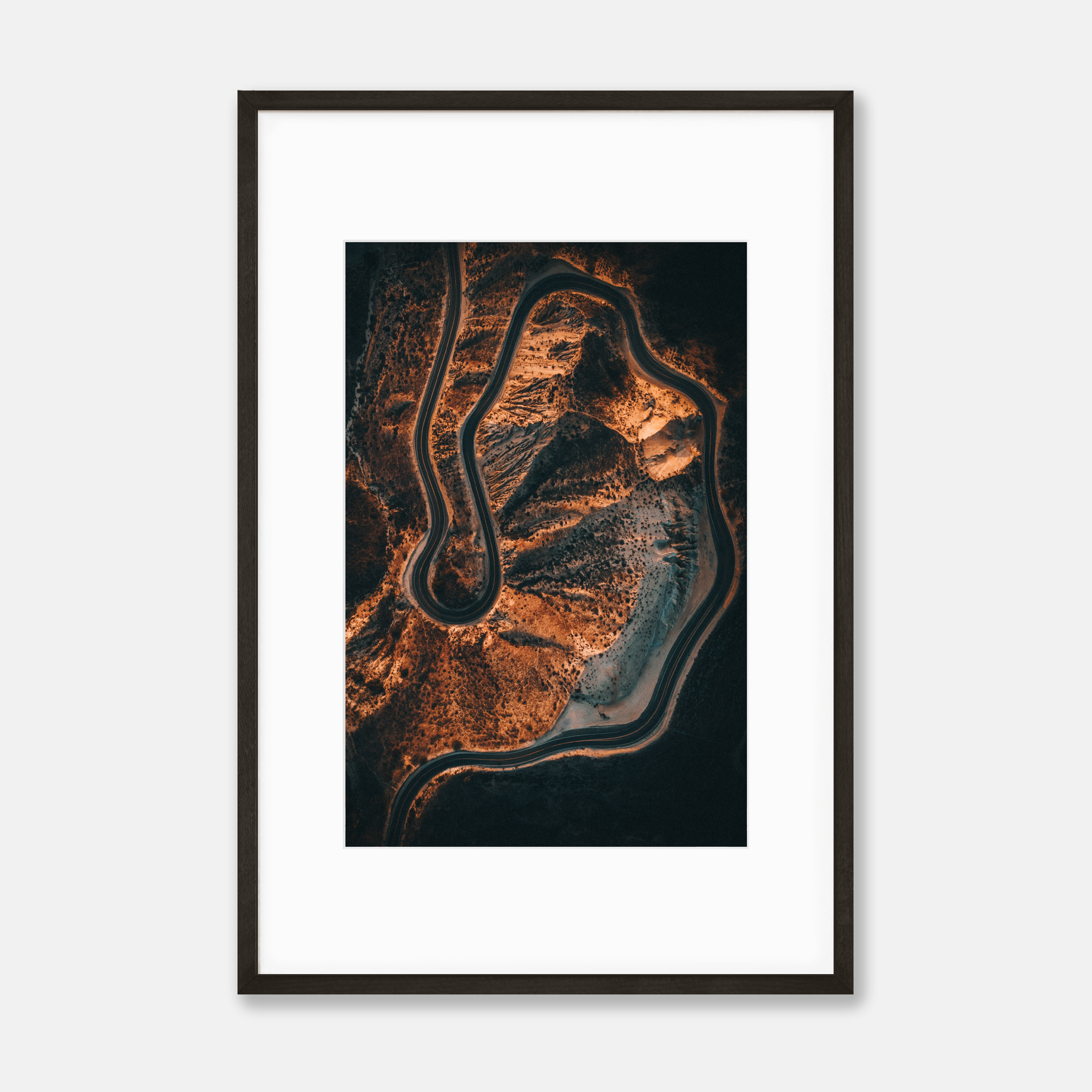 Aerial view of a winding mountain road through a rugged landscape with trees and exposed terrain, during sunset or sunrise with warm orange lighting.