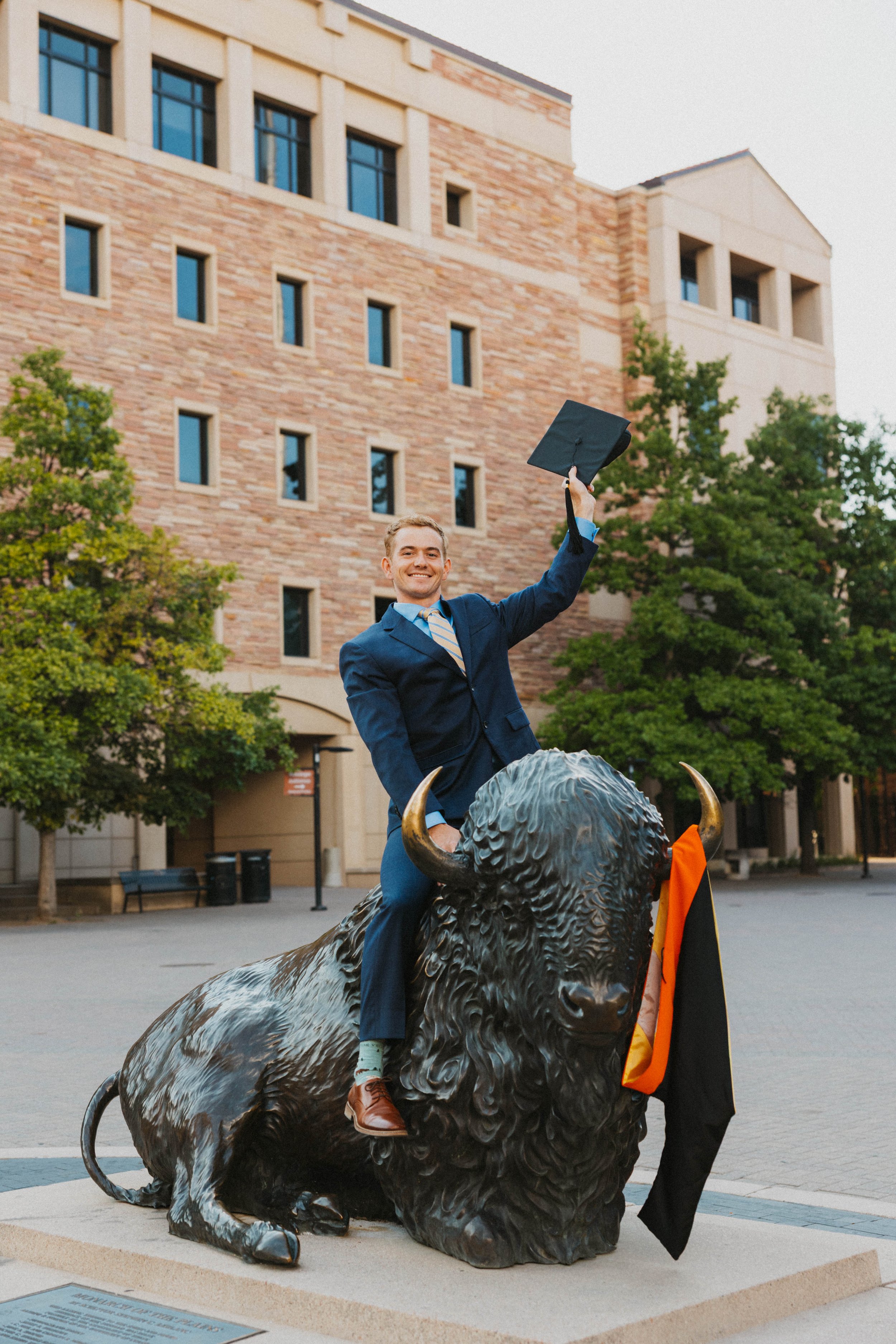 Boulder Graduate on Mascot holding cap in the air