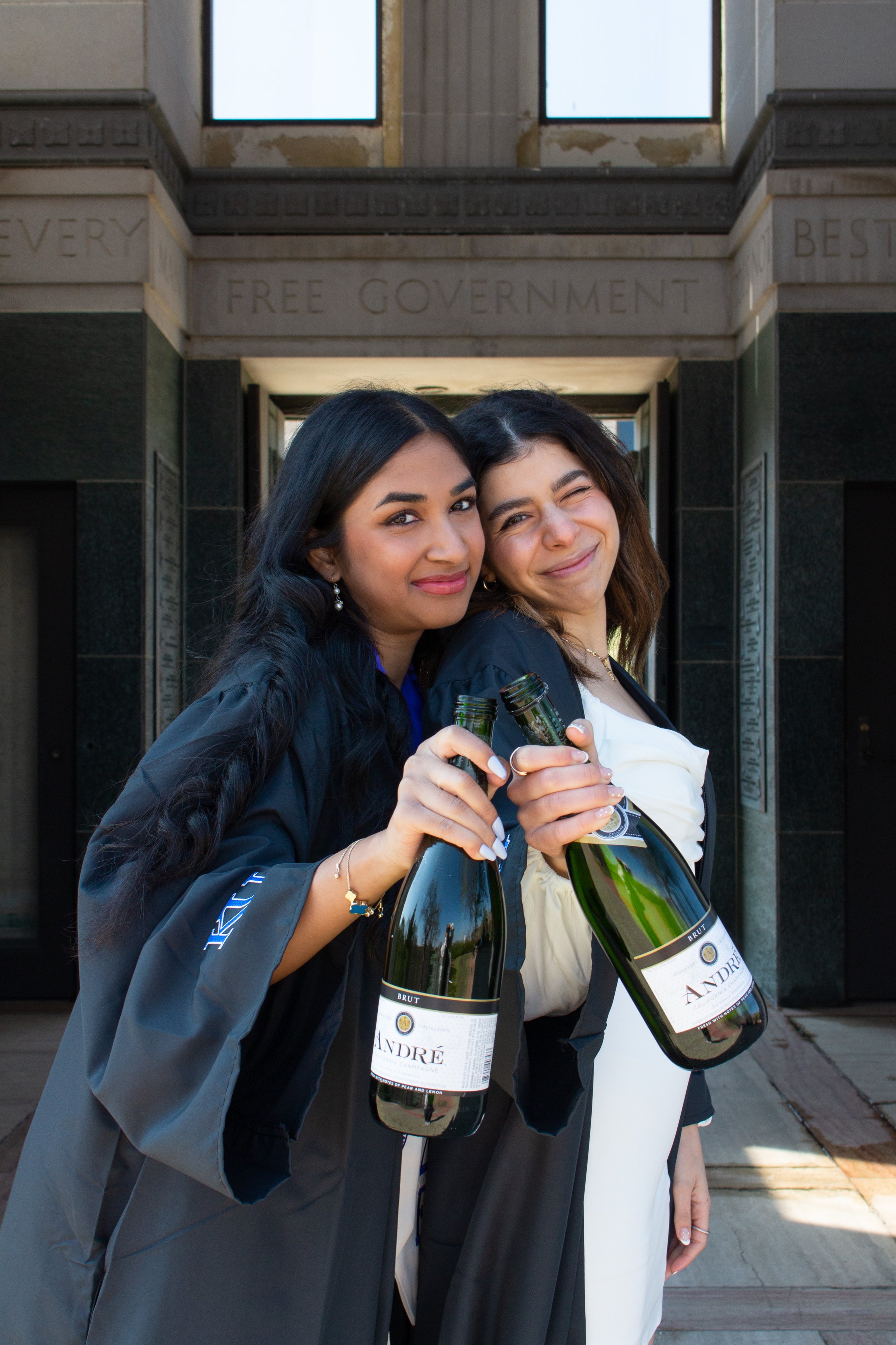 Two girls clink champagne for grad pictures at KU