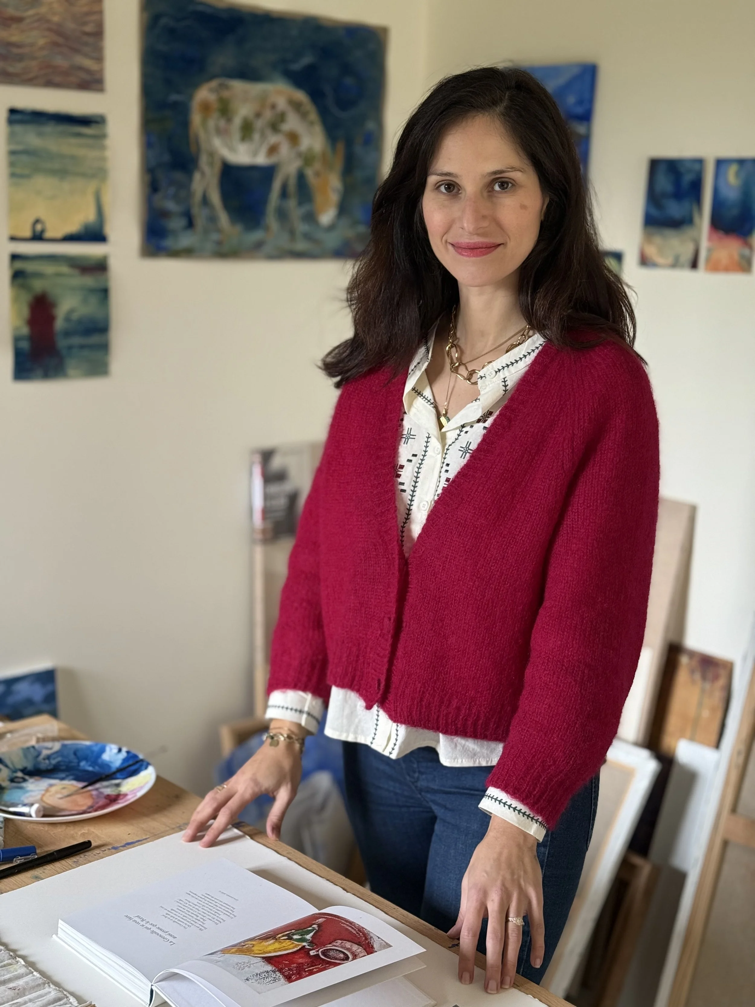 Portrait de Jeanne-Sophie de Peretti debout à côté d'une table dans son atelier d'art, entourée de peintures accrochées au mur.