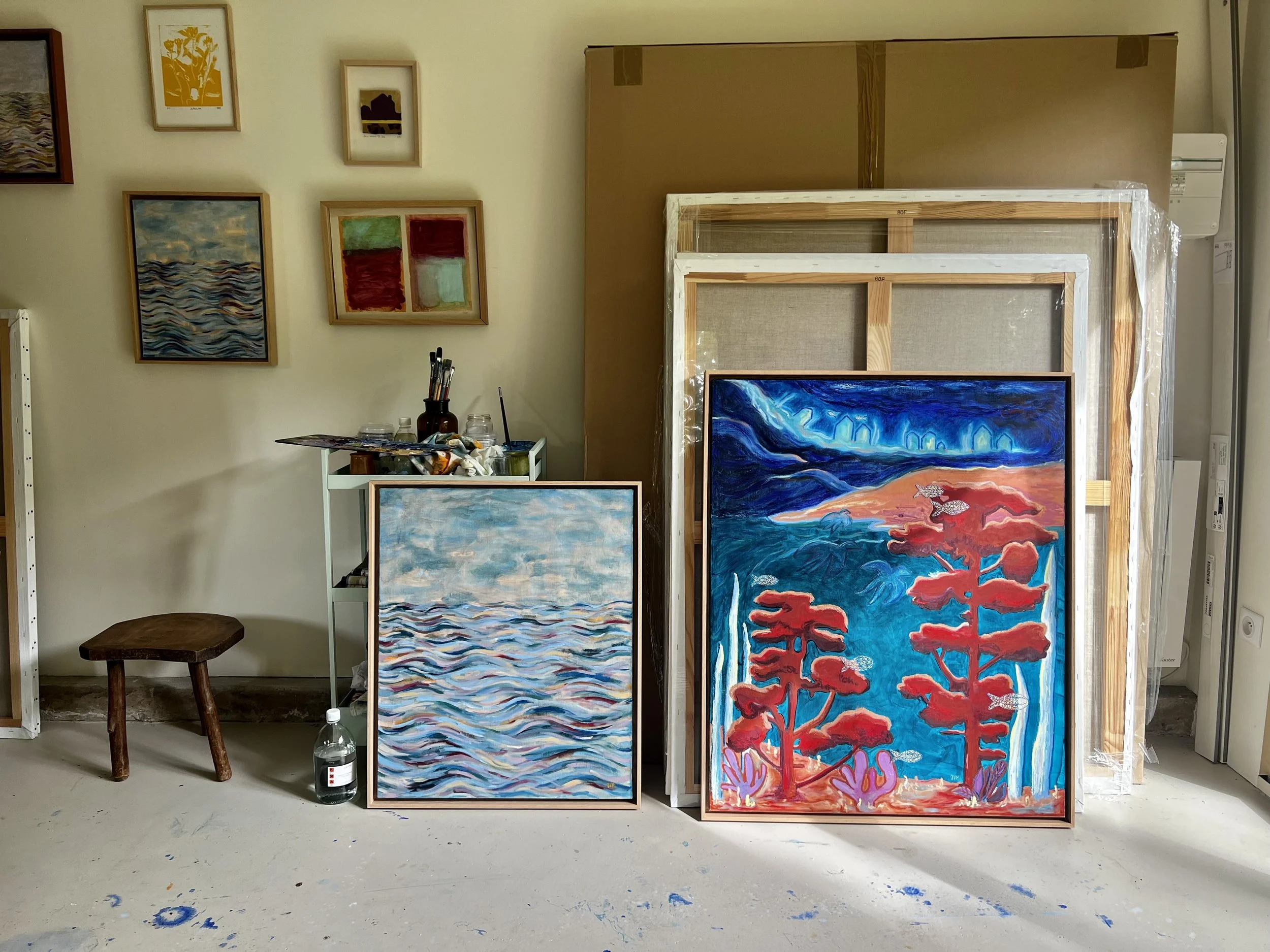 Atelier d'art de Jeanne-Sophie de Peretti avec plusieurs peintures, y compris deux grandes toiles avec des paysages de nature et avec des oeuvres d'art décorant le mur.