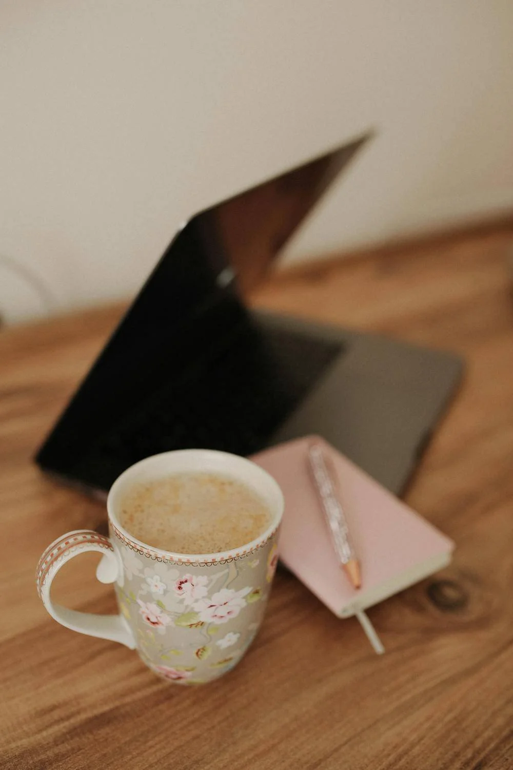 Laptop einer Webdesignerin mit geblümter Kaffeetasse und rosa Notizbuch