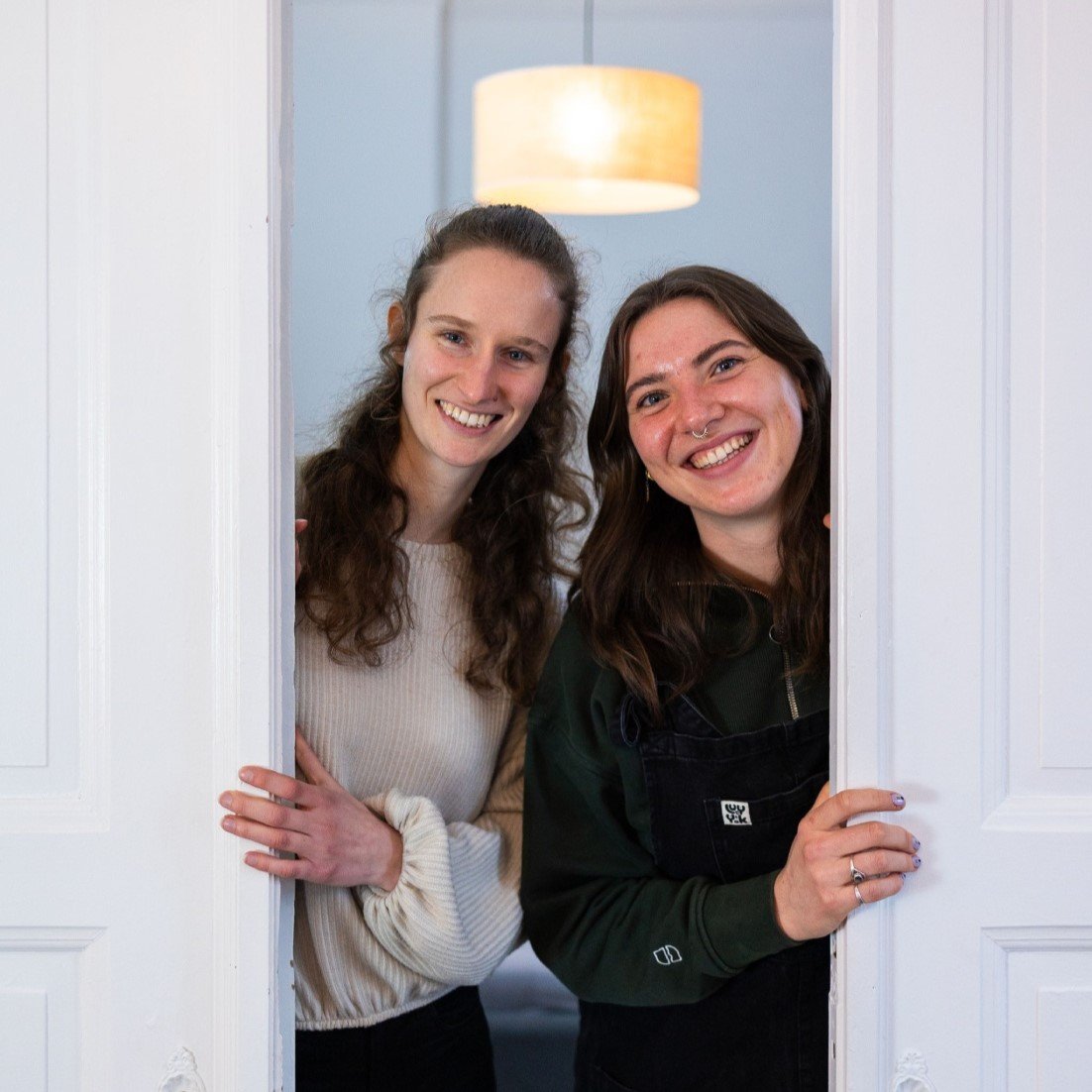 Webdesignerinnen schauen lächelnd hinter weißer Tür hervor