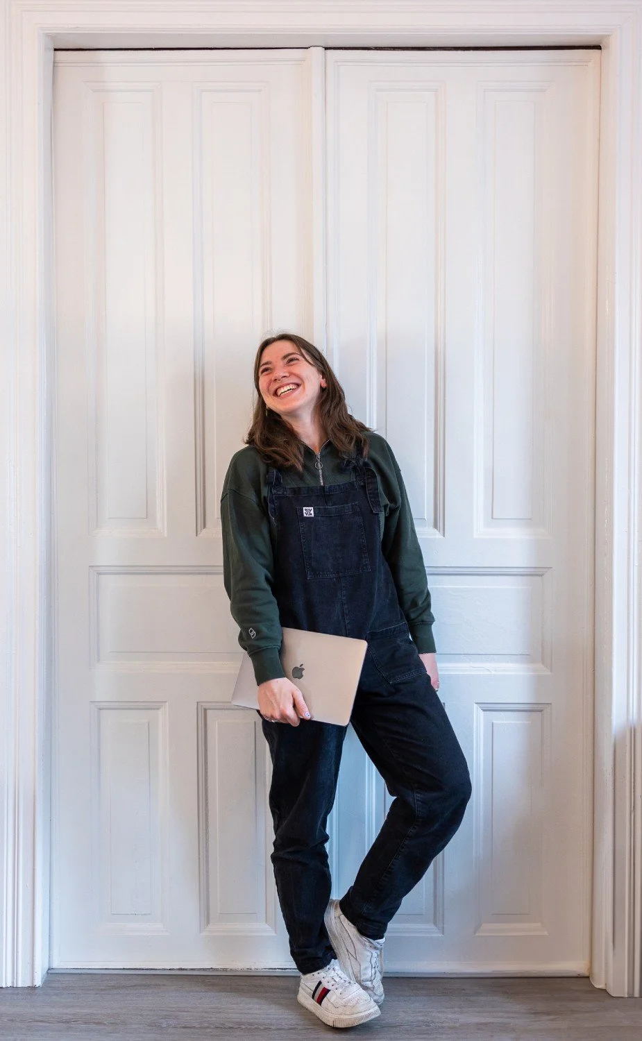 Franzi lächelnd mit Laptop vor weißer Tür