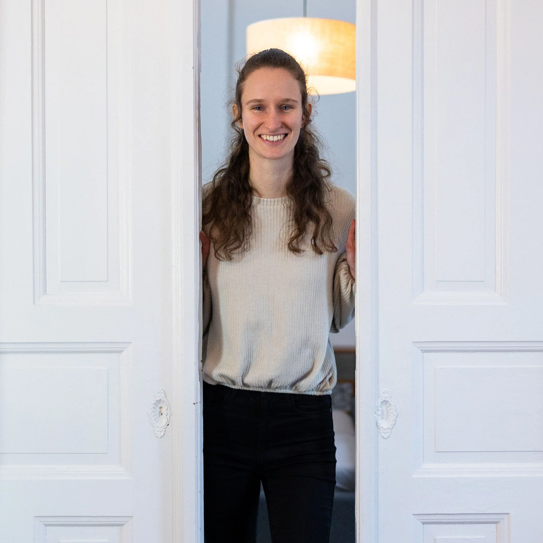 Webdesignerin Maike von Maia Studio schaut zwischen zwei weißen Altbautüren hervor