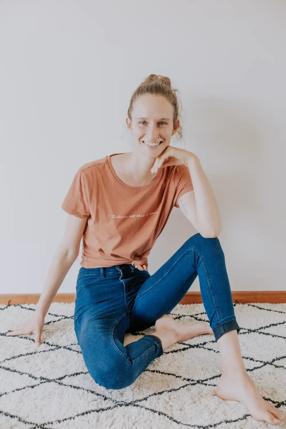 Squarespace Partner Maike sitzt mit braunem T-Shirt und Jeans vor Wand