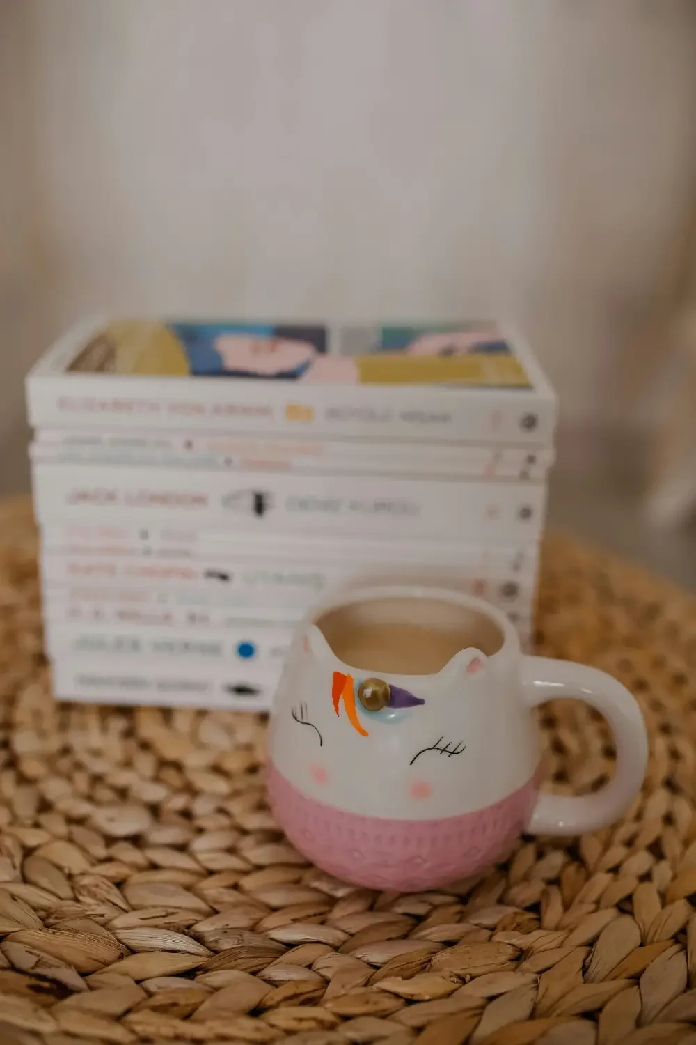 Einhorntasse neben Bücherstapel auf Rattanunterlage