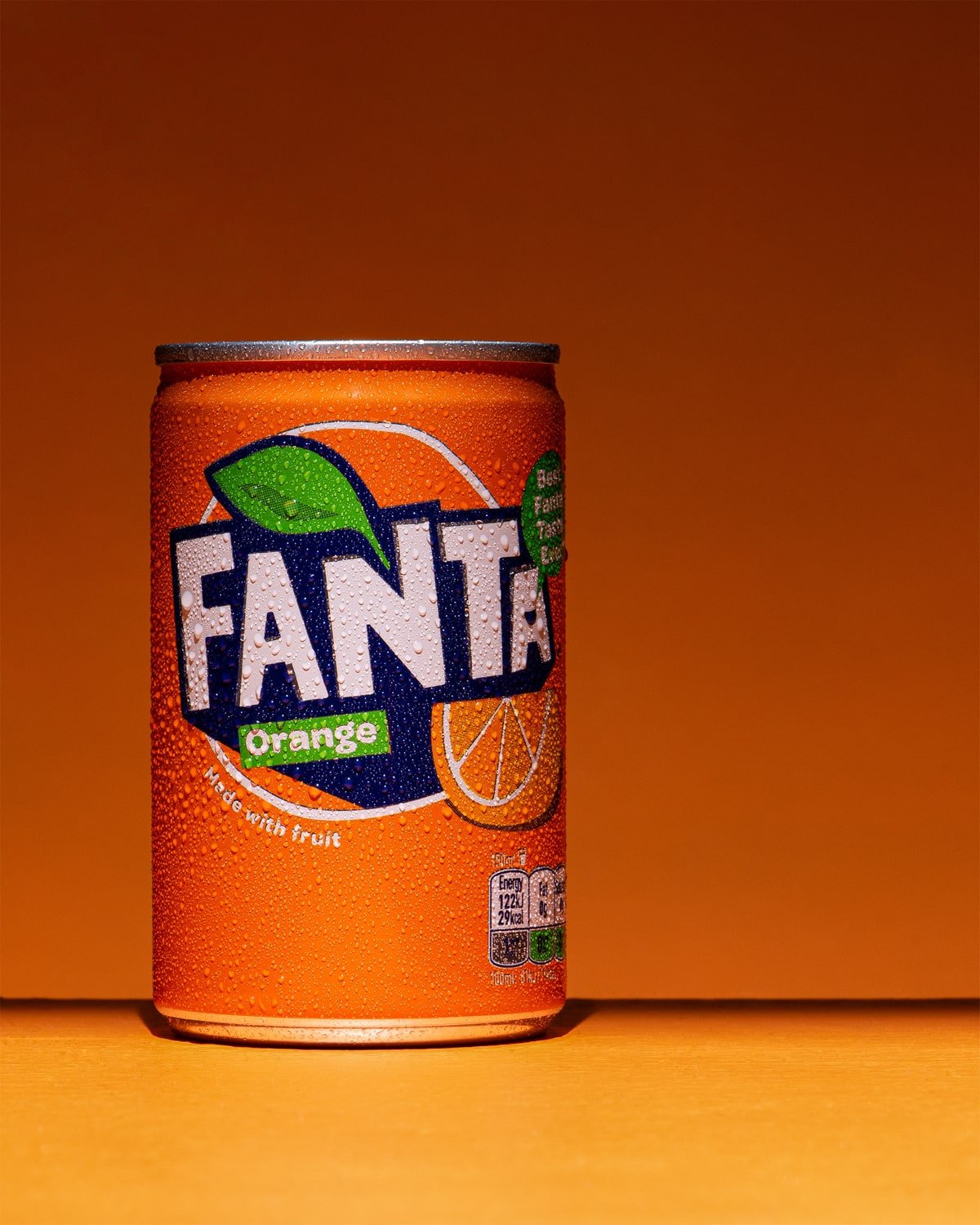 Soft drink product photo showing a can of Fanta against an orange background. A can of Orange juice.