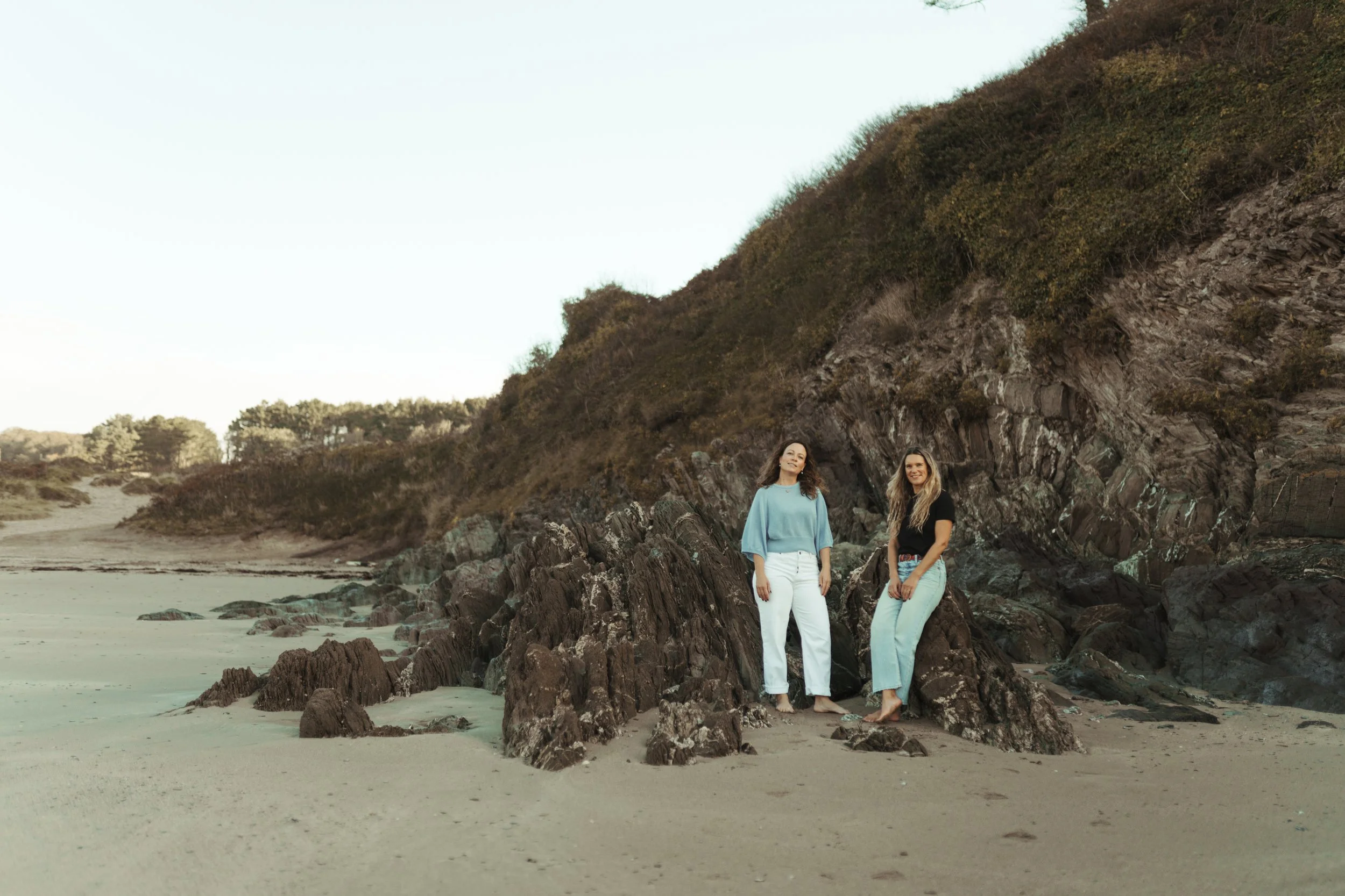 Two women sitting on stone steps outdoors, smiling at the camera, in casual attire with one in a sweater and the other in a sweatshirt.