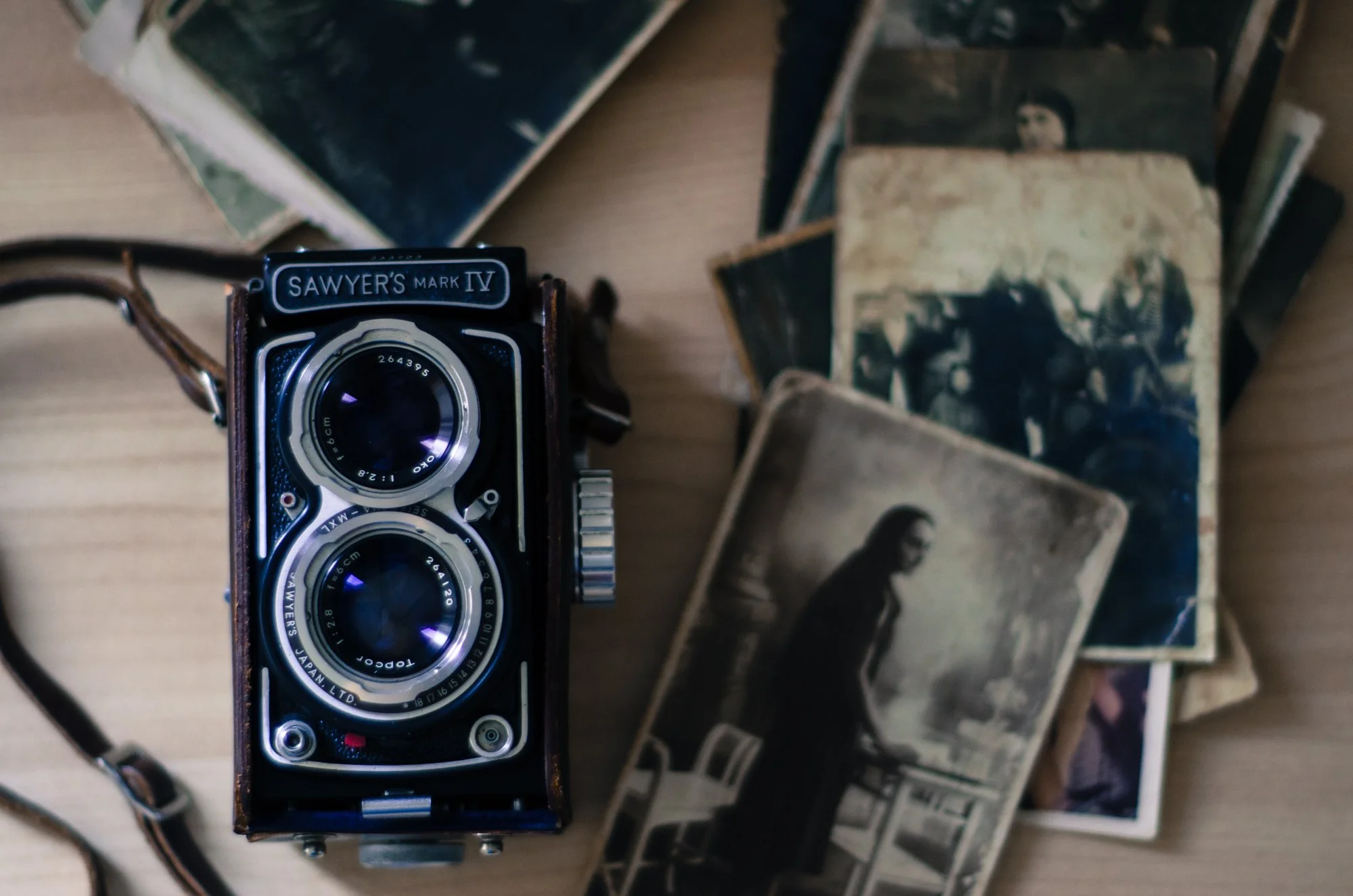 Vintage twin-lens reflex camera next to old black-and-white photographs on a wooden surface.