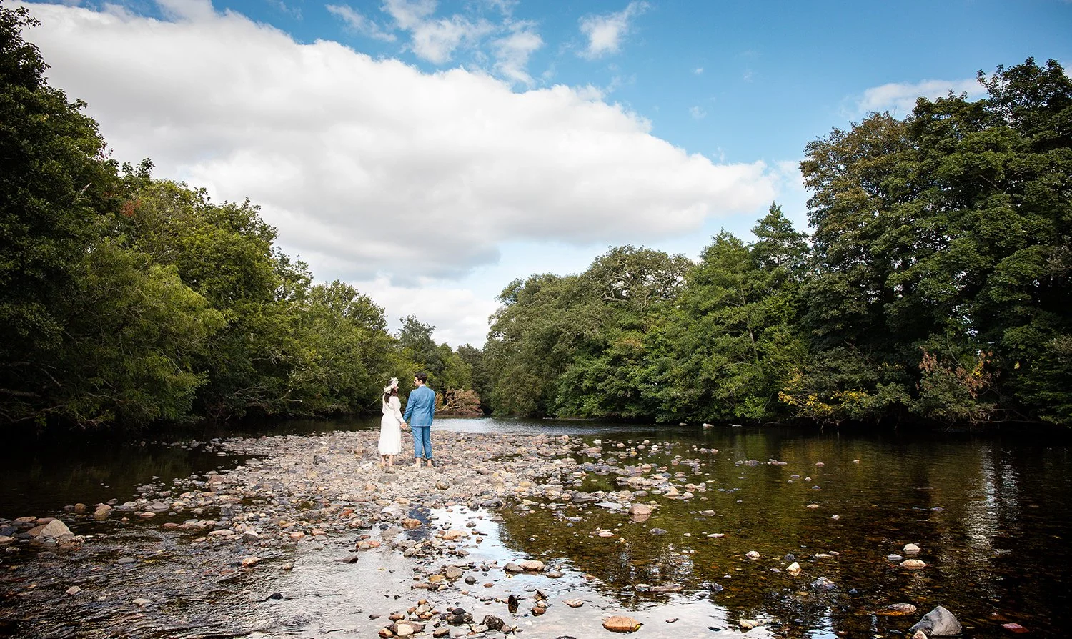 bride and groom standing on the bank of a river in devon