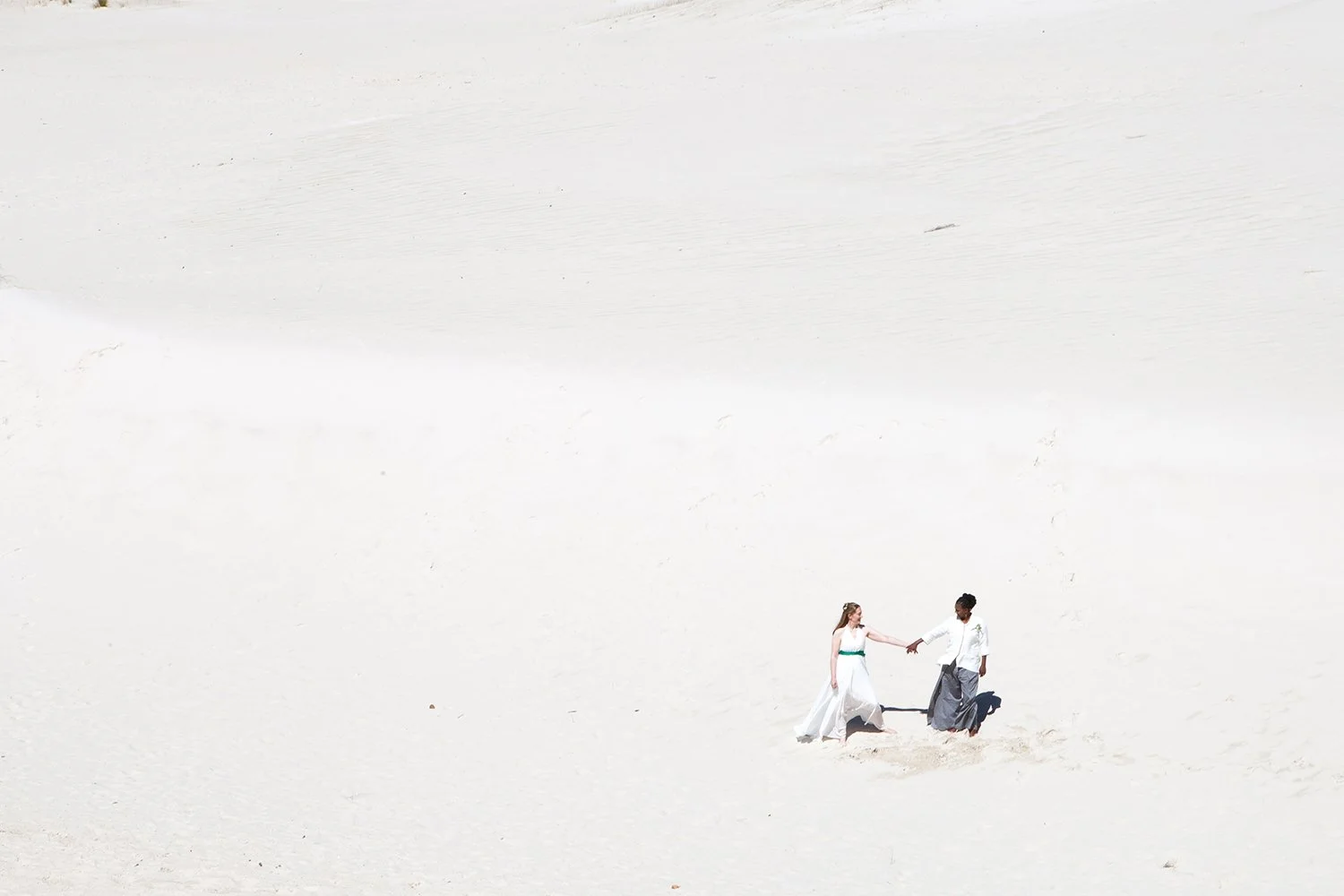 same sex couple holding hands in sand dune