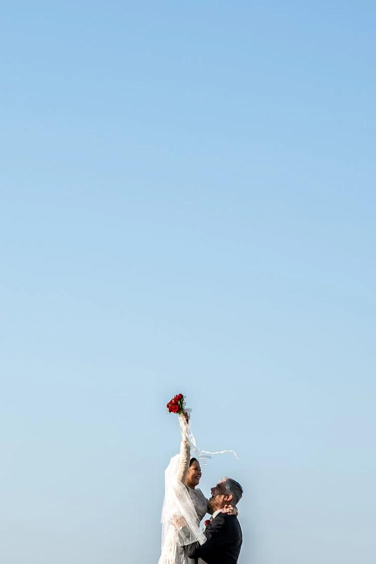 Bride and groom after getting married in Devon, the sky is bright blue and the bride is holding up a bouquet of flowers