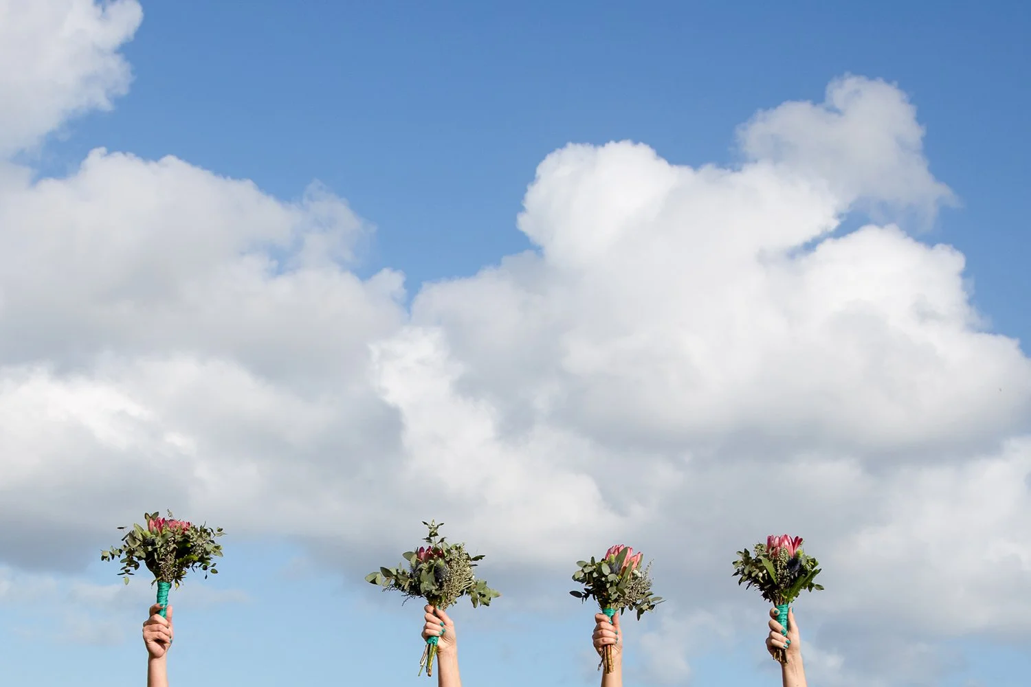 hands holding wedding flowers with blue skies and clouds in background