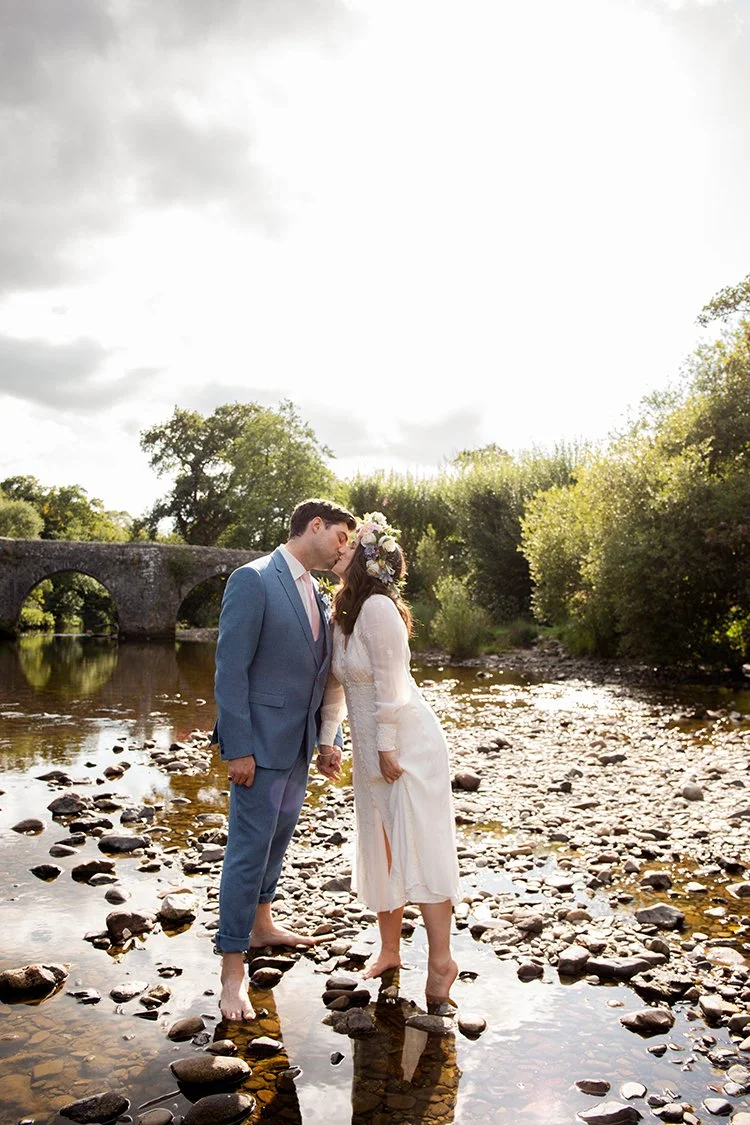 bride and groom bare footed in river in devon kissing