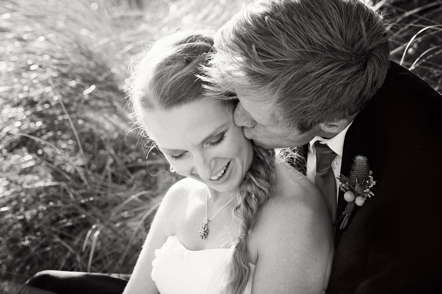groom kissing bride sitting in dune