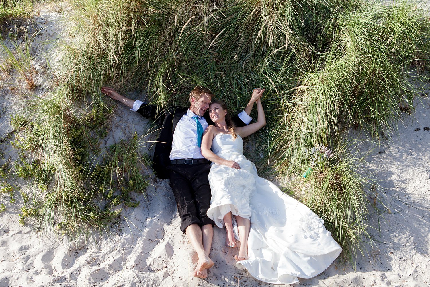 bride and groom lying in sand dunes