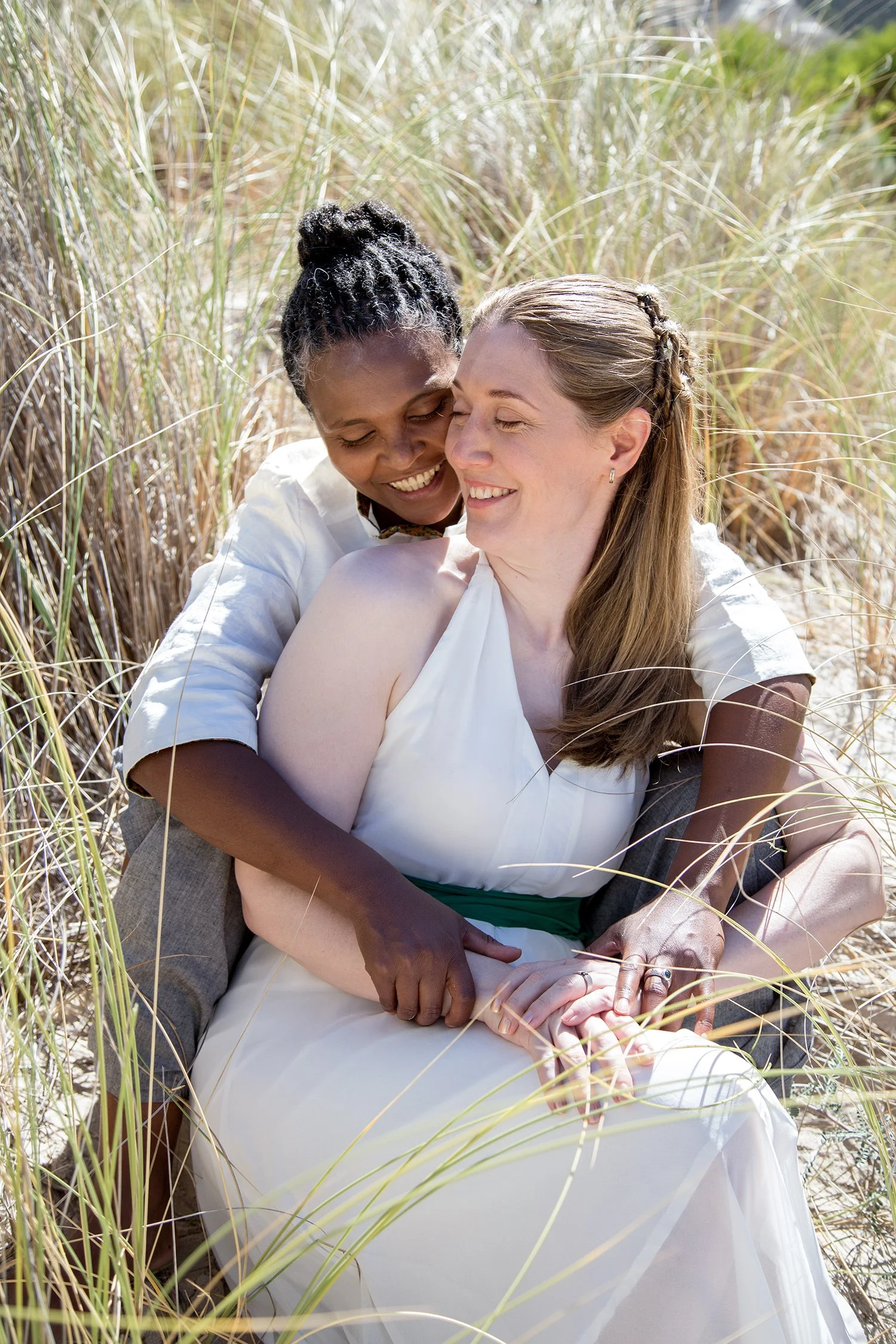 same sex wedding couple holding hands sitting in sand dune