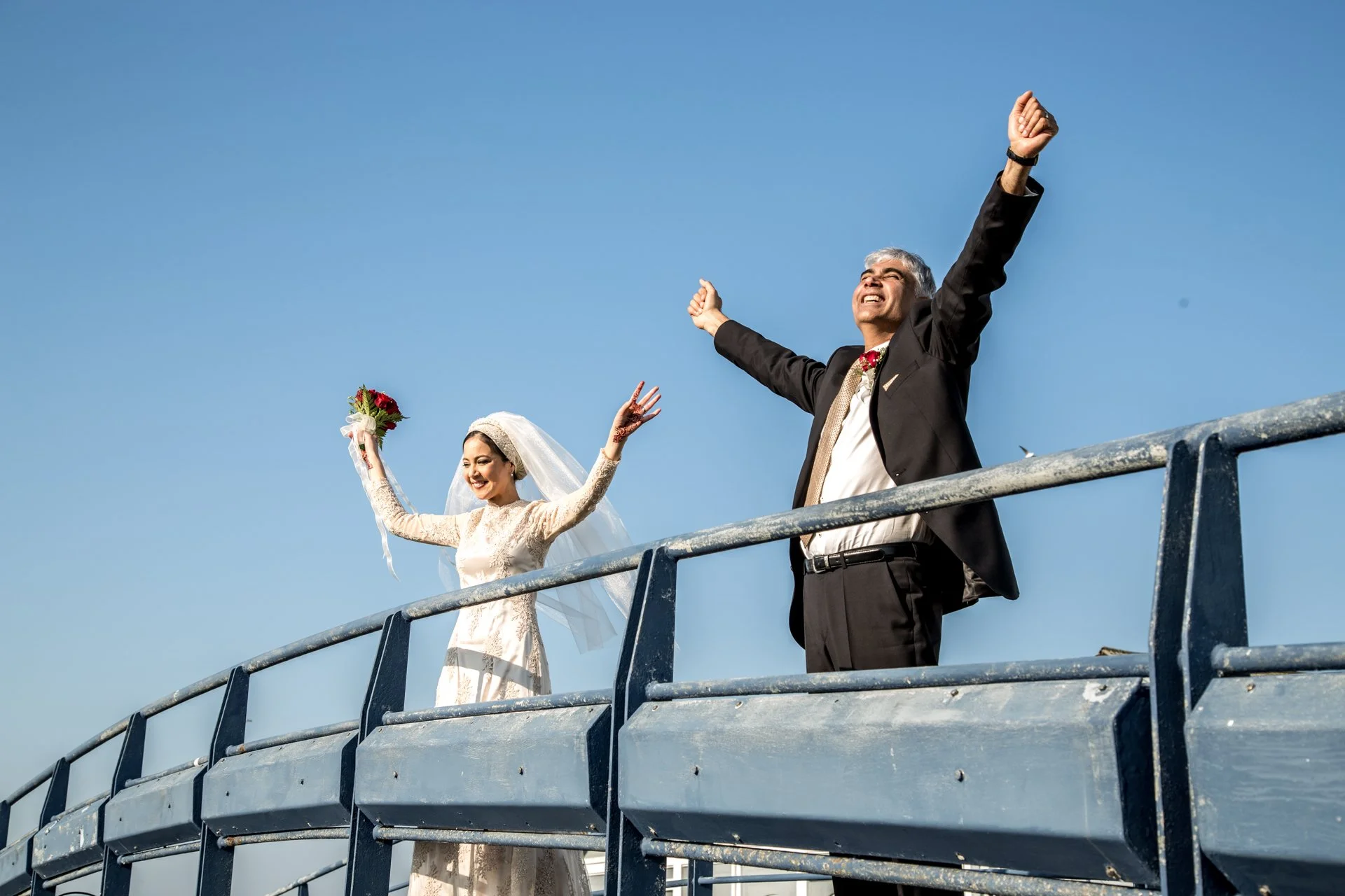 bride and groom with hands up in air on bridge