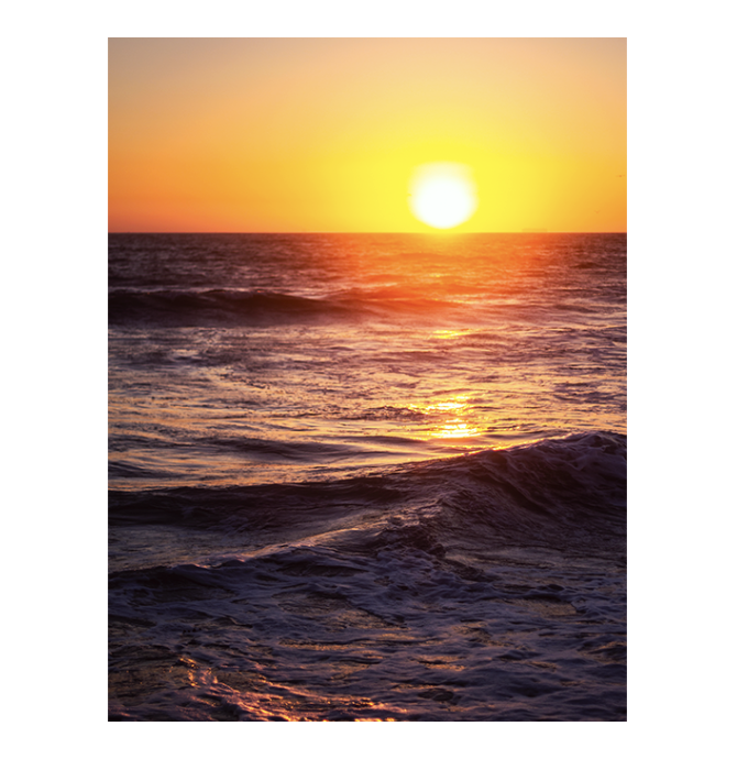 Sunset over the ocean with waves and reflections of the sun on the water.