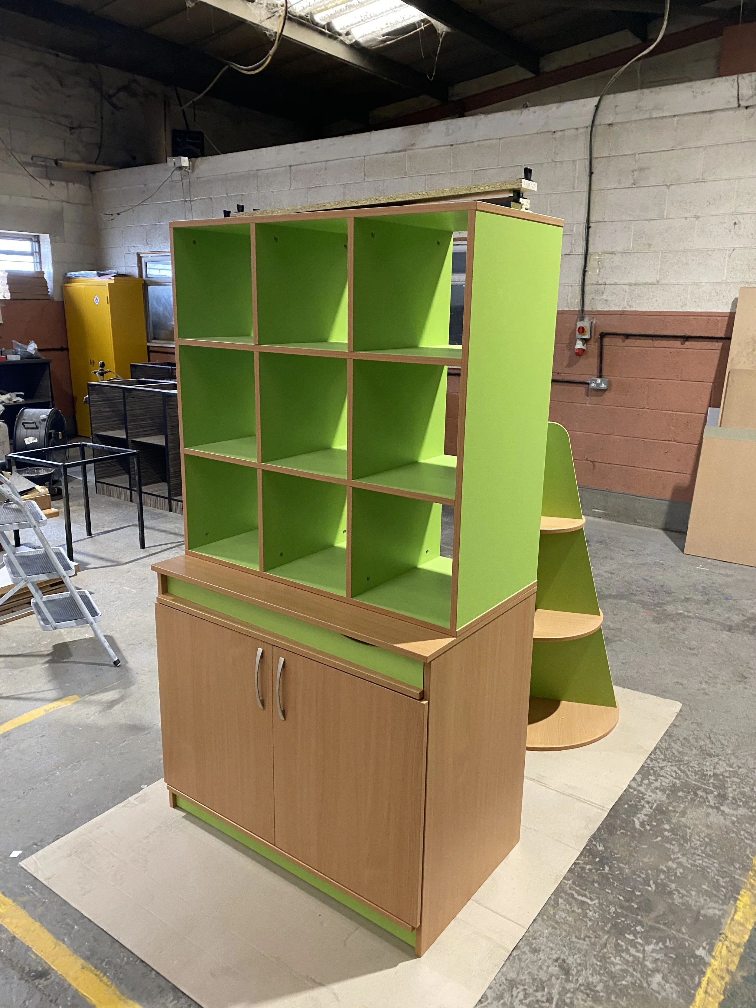 A multi-level wooden and green shelving unit with cubbies and a cabinet in a workshop.