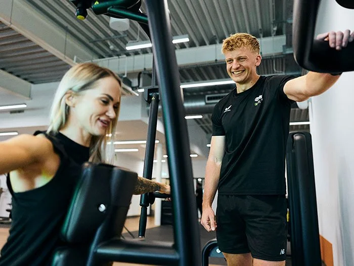 Personal trainer coaching client on gym equipment in franchise setting